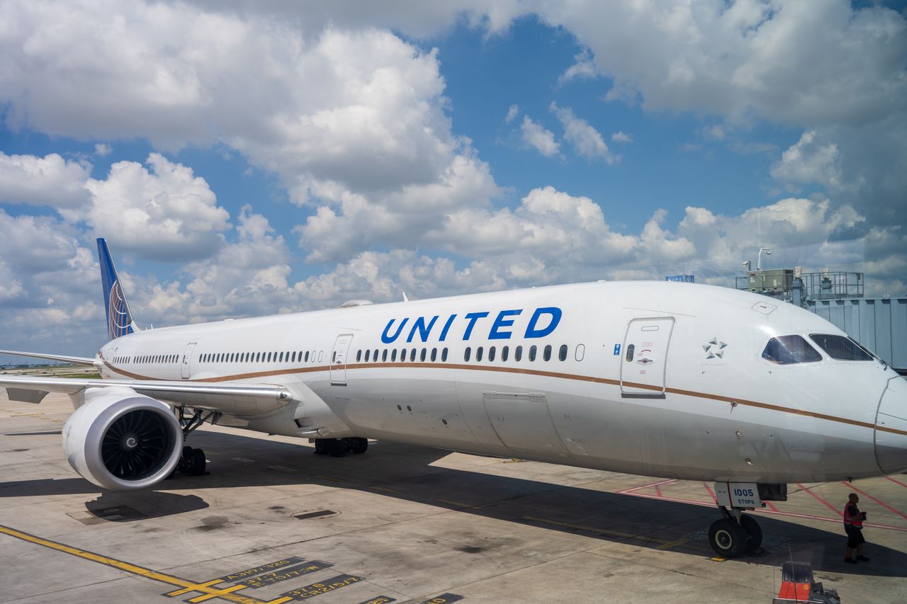 A United Airlines Boeing 787 aircraft parked at the airport terminal under a bright blue sky with clouds.